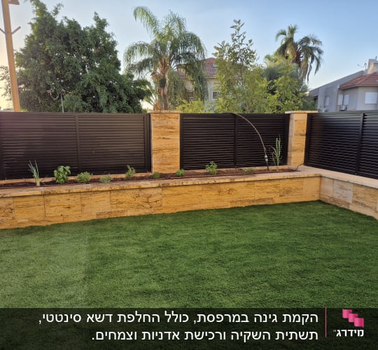 גינה עם דשא ירוק וצמחים בגדר אבן